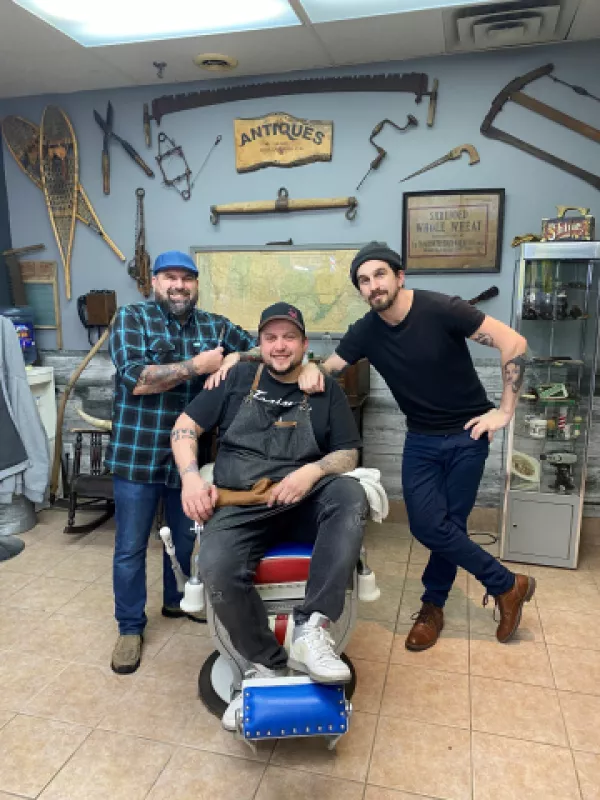 Barber sitting in barber chair with colleague on either side 