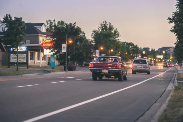 Vintage car driving away down a road at dusk