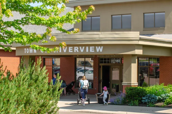 A mother pushing a stroller into the library on a summer day with another child walking beside them