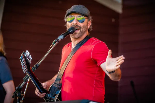 Singer in a red shirt and sunglasses singing into microphone