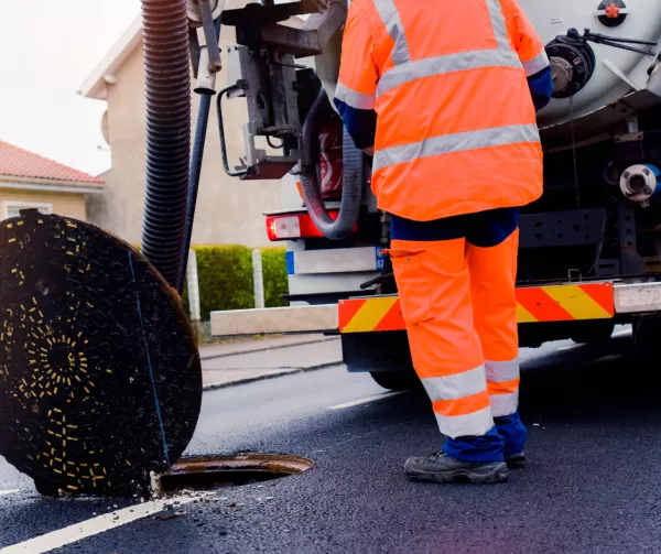 Sewer cleaning truck person standing beside drain