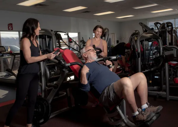 Person using shoulder press machine with employee support