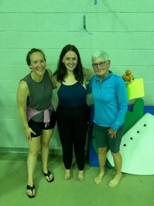 recipient of scholarship stands on pool deck with current and past aquatics coordinators