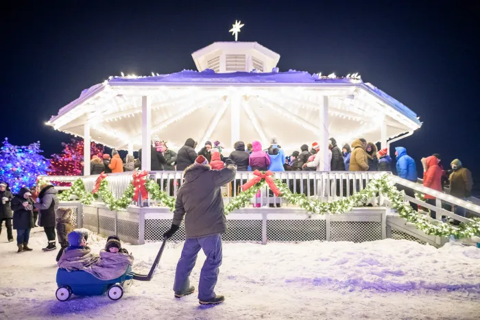 Gazebo lit up with holiday lights and people gathered.